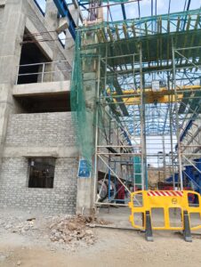 Building entry with yellow scaffolding and netting for pipeline housing.