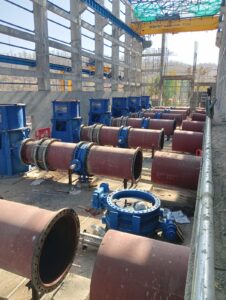 Large steel pipelines, valves, and fittings laid out at the site.
